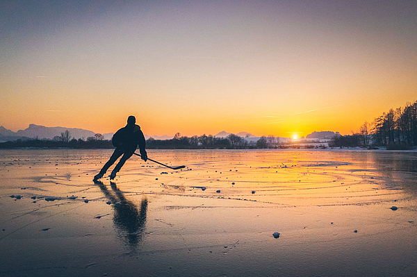 Eishockeyspieler bei Sonnenuntergang auf zugefrorenem See