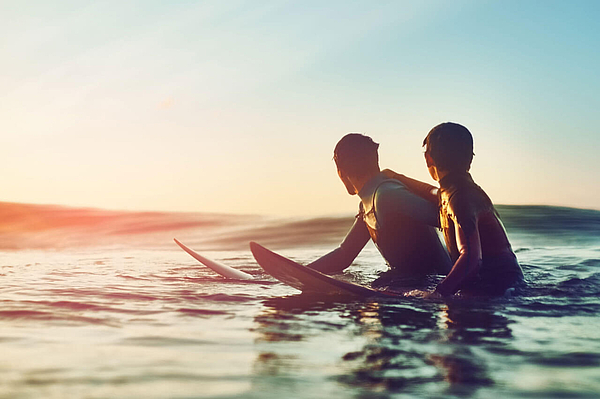 Zwei Surfer im Abendlicht auf dem Wasser.