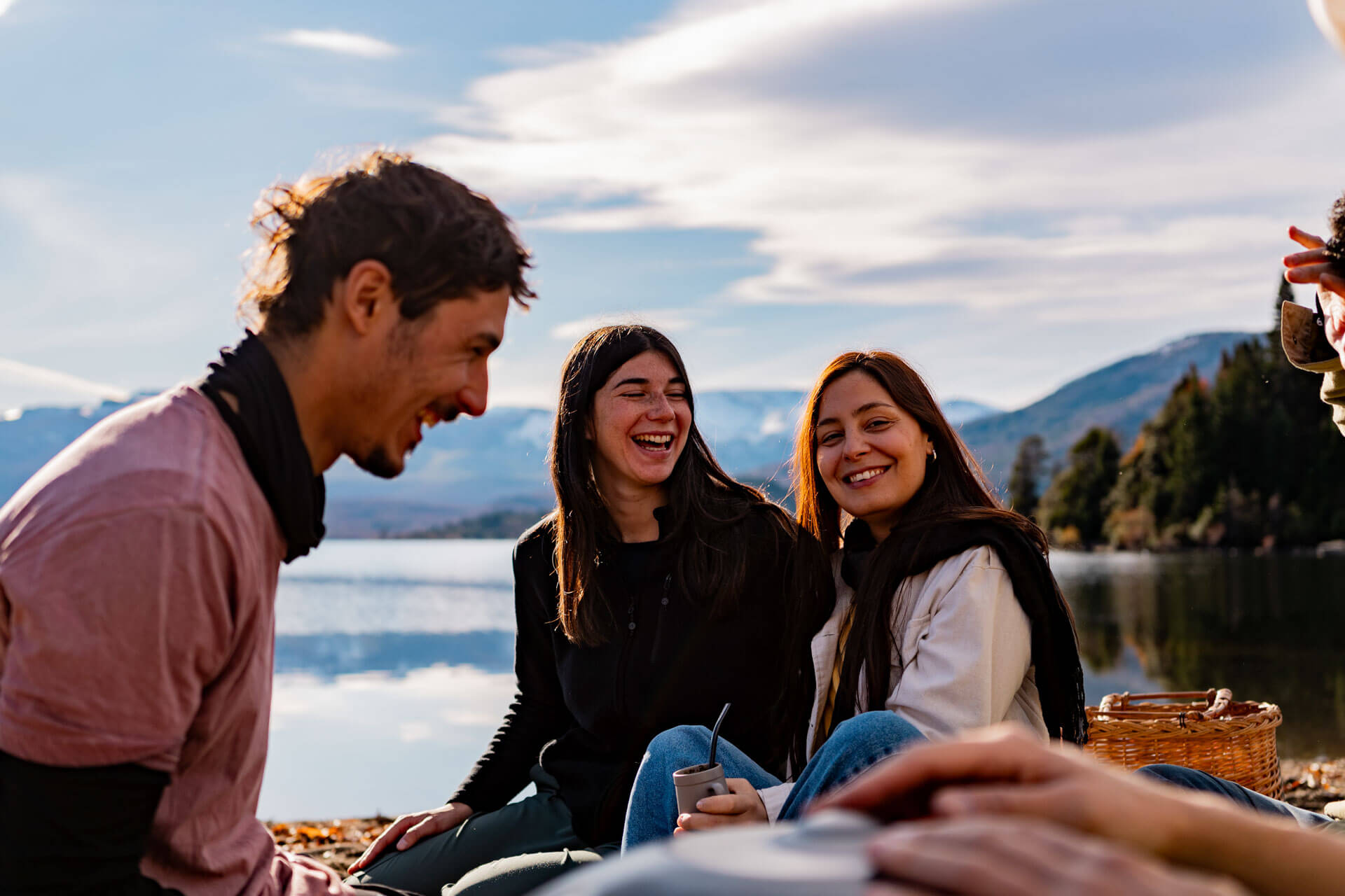 Gruppe junger Erwachsener lacht gemeinsam am Seeufer mit Blick auf die Berge bei Mendoza