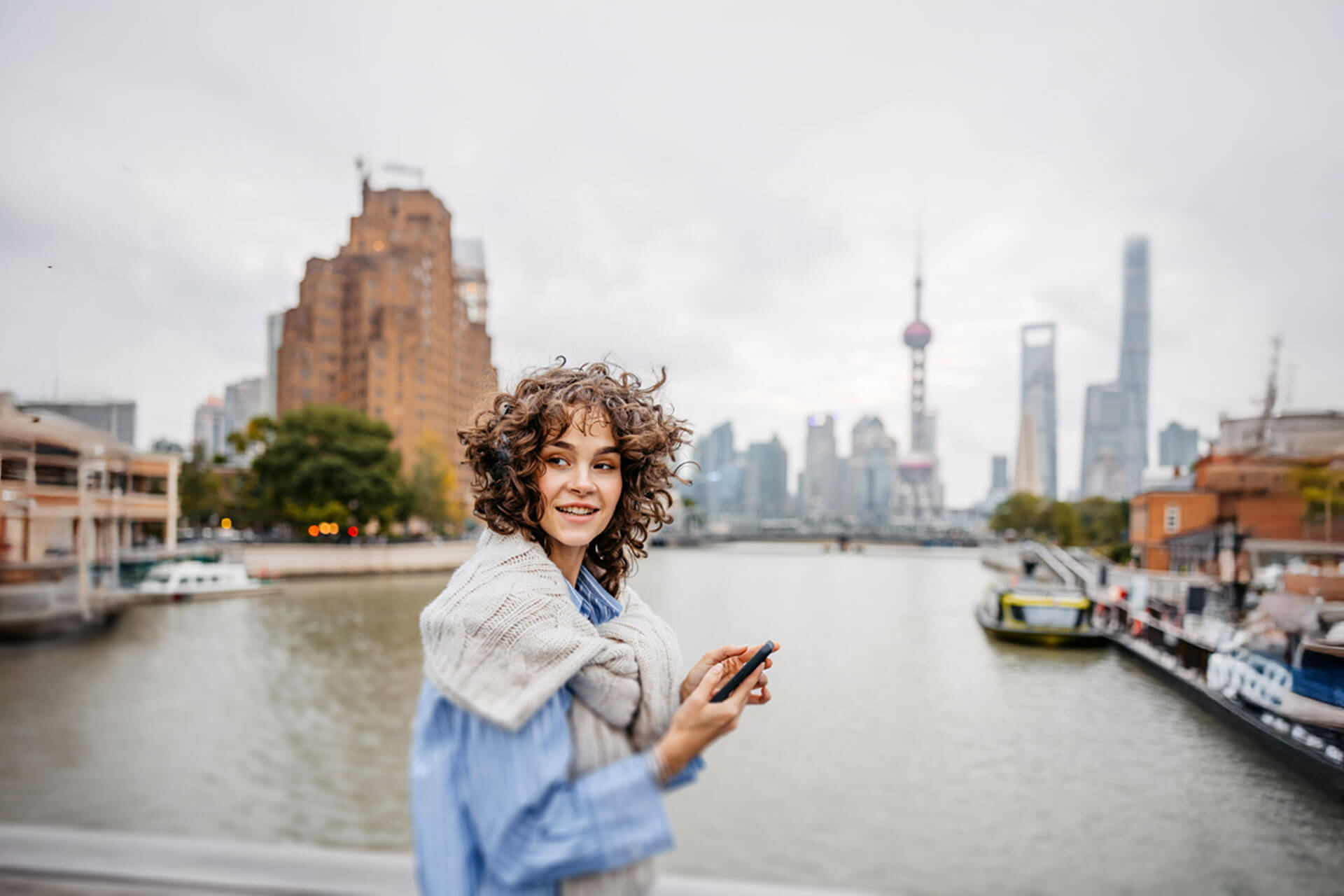 Person steht an einem Flussufer in Shanghai mit Blick auf die Skyline und den Oriental Pearl Tower