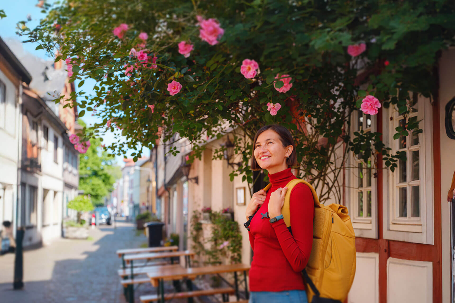 Person mit gelbem Rucksack lächelt auf blühender Altstadtstraße in Frankfurt