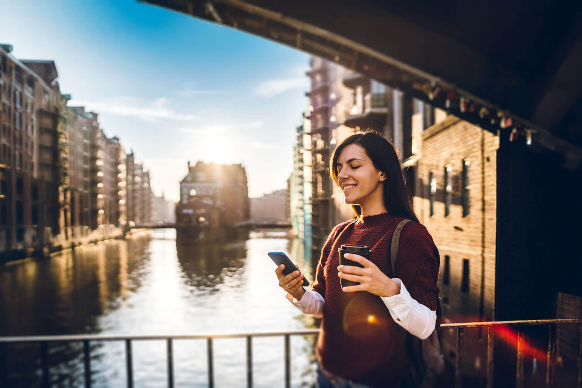 Person mit Smartphone und Kaffeebecher steht auf einer Brücke in der Speicherstadt Hamburg