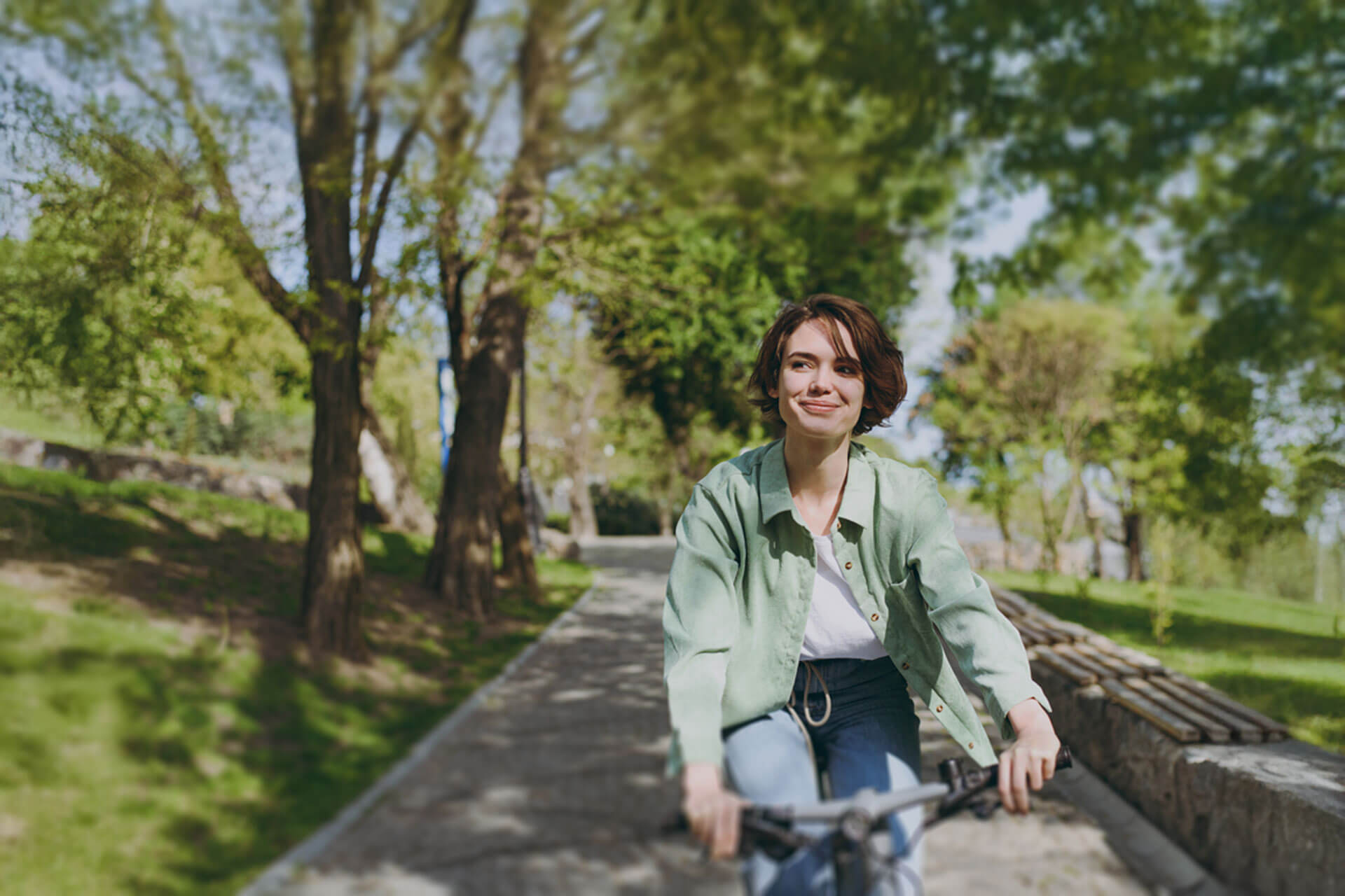 Person fährt lächelnd mit dem Fahrrad durch einen grünen Park in Münster