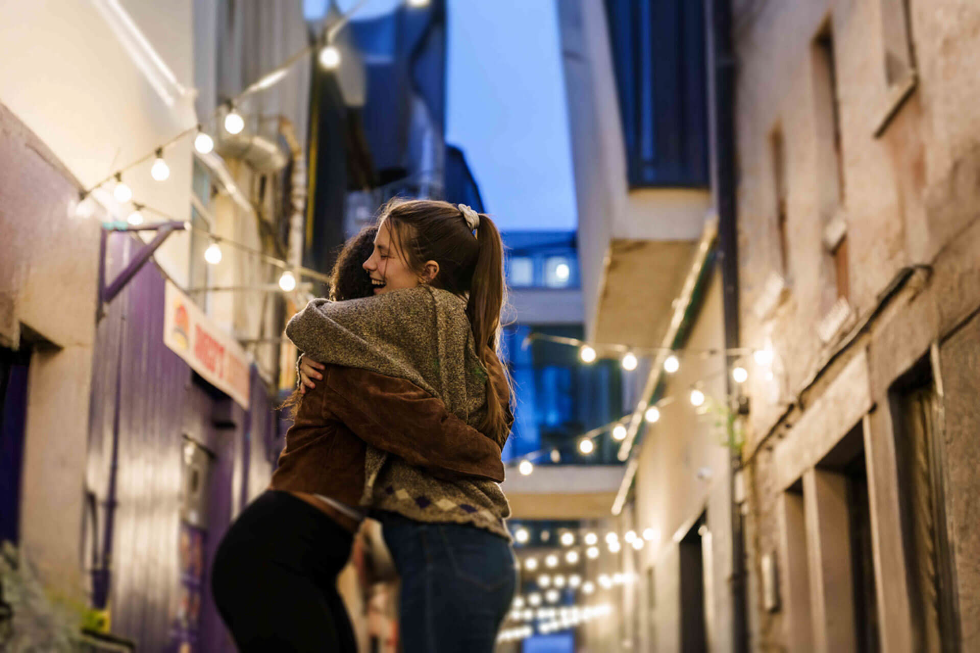 Zwei Freundinnen umarmen sich in einer stimmungsvoll beleuchteten Gasse am Abend in Canterbury
