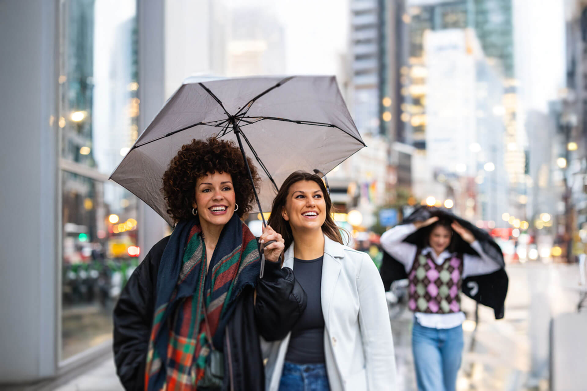Zwei Personen gehen lachend mit Regenschirm durch eine belebte Straße in einer britischen Stadt an einem regnerischen Tag