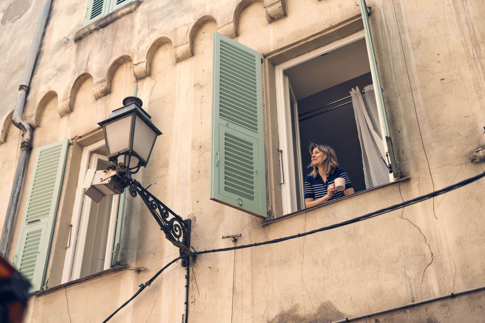 Frau blickt aus dem Fenster eines historischen Gebäudes in Montpellier während ihres Sprachaufenthalts