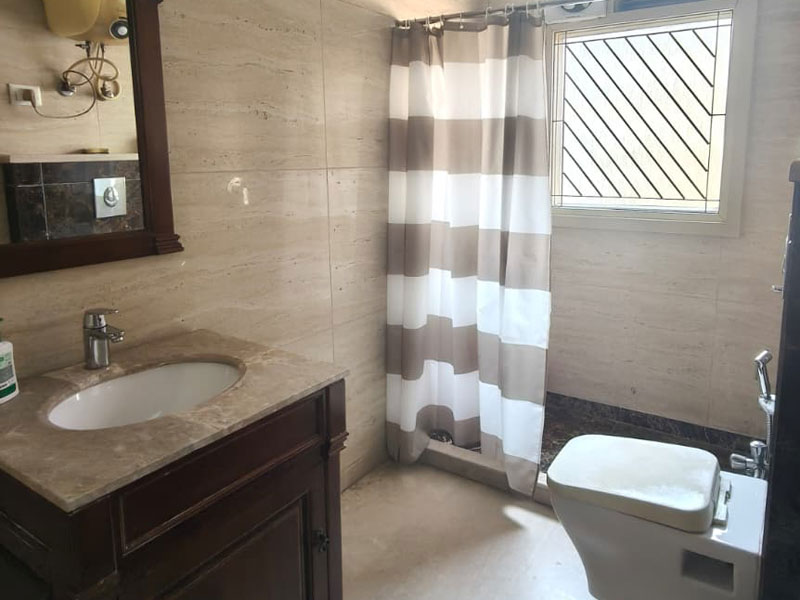 Badezimmer im Apartment in Neu-Delhi mit Dusche, Waschbecken und Fenster.