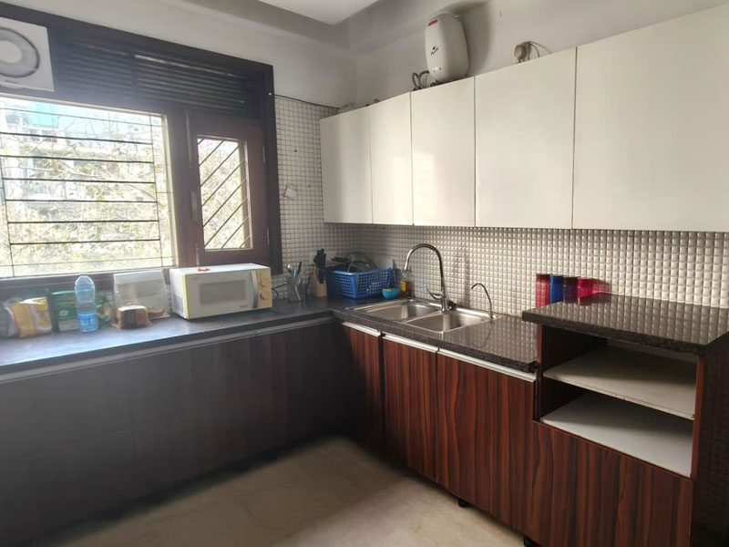 Küche im Apartment in Neu-Delhi mit Spüle, Mikrowelle und Stauraum für Selbstverpflegung.