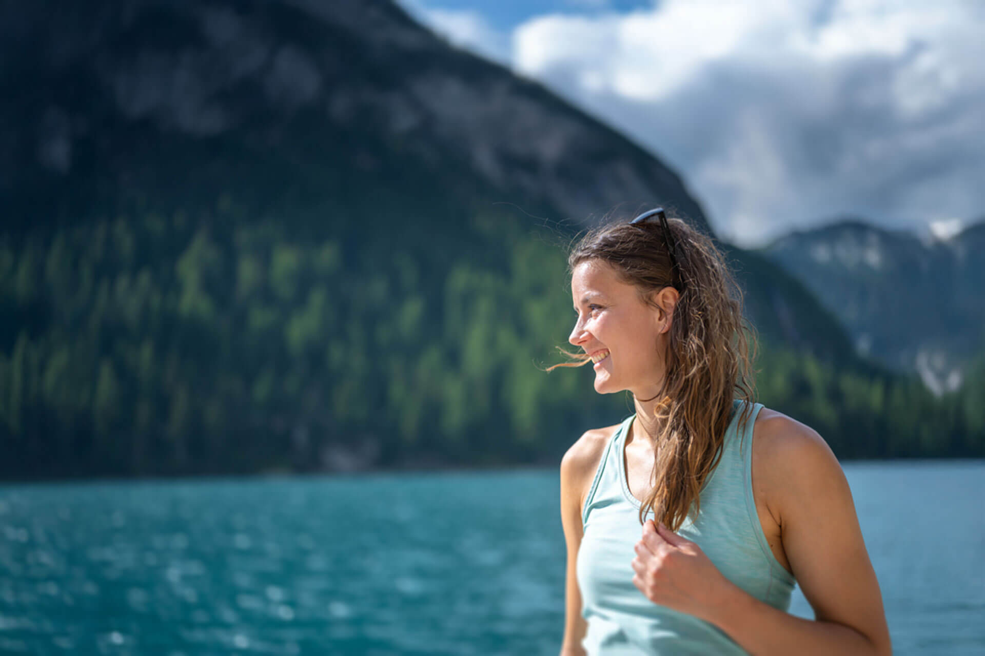 erson steht am türkisblauen See vor Bergkulisse und genießt die Natur in der Sonne