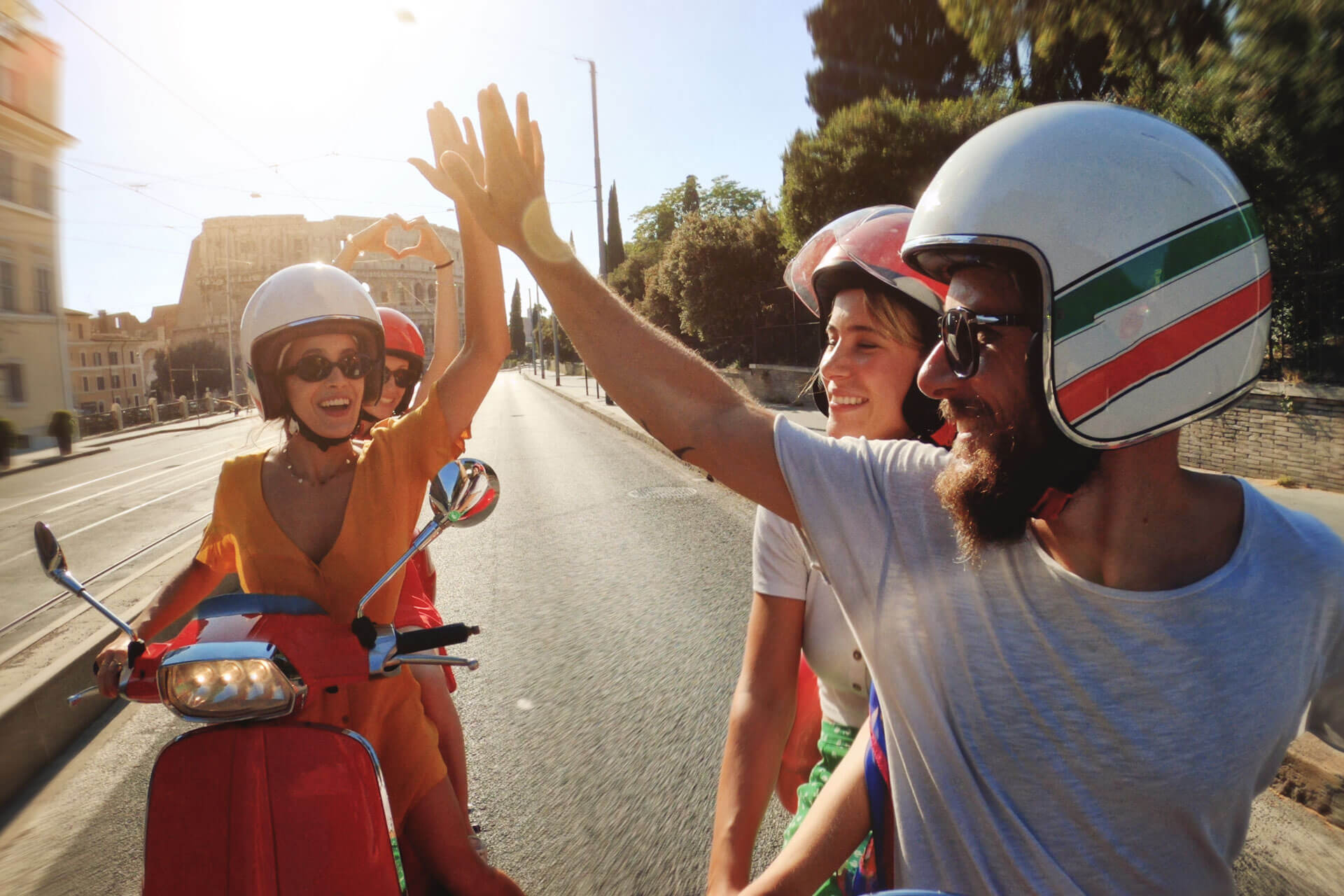 Gruppe junger Menschen fährt lachend auf Motorrollern durch Rom und gibt sich ein High-Five