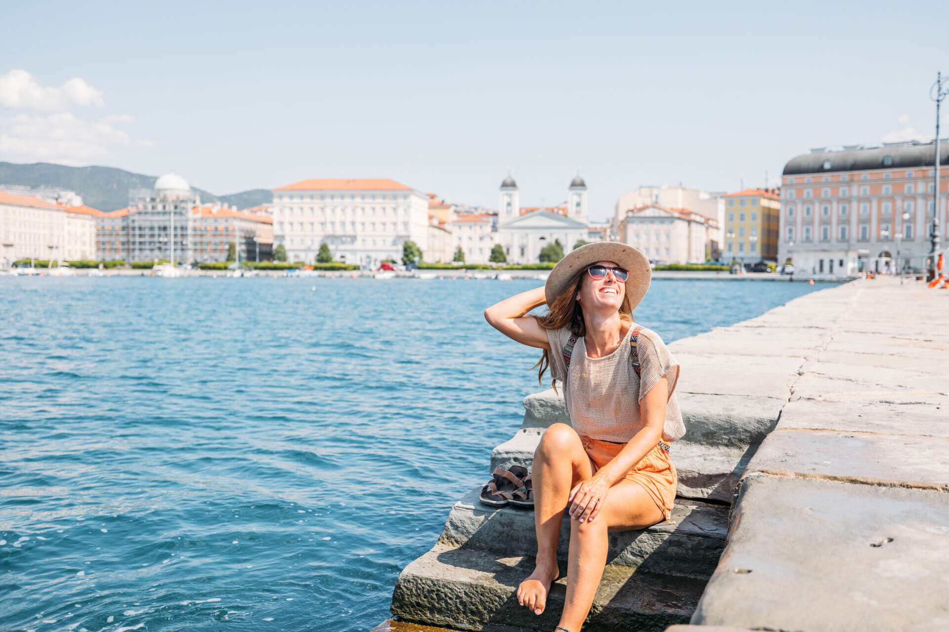 Person sitzt entspannt an der Uferpromenade von Triest mit Blick auf das Meer und die historischen Gebäude der Stadt