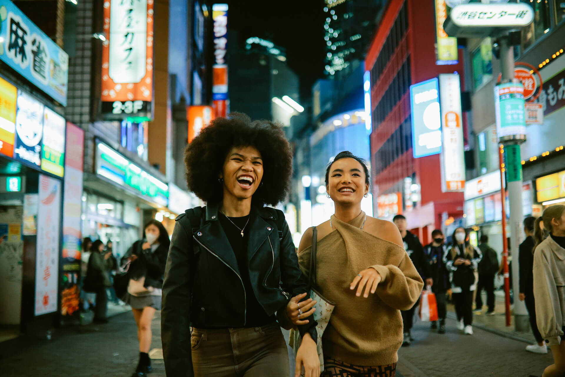 Zwei Personen lachen beim Spaziergang durch Tokios belebte Straßen mit bunten Leuchtreklamen am Abend