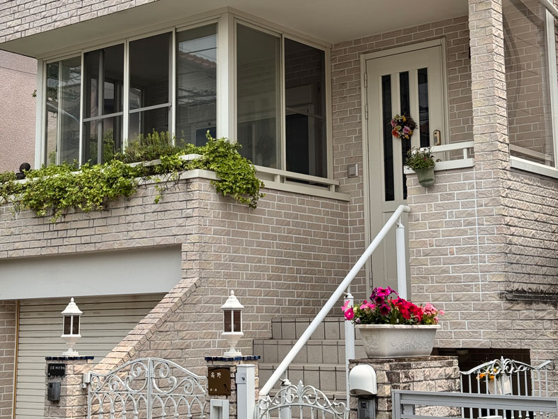 Eingang eines japanischen Wohnhauses in Tokio mit Balkon, Blumen und heller Backsteinfassade.