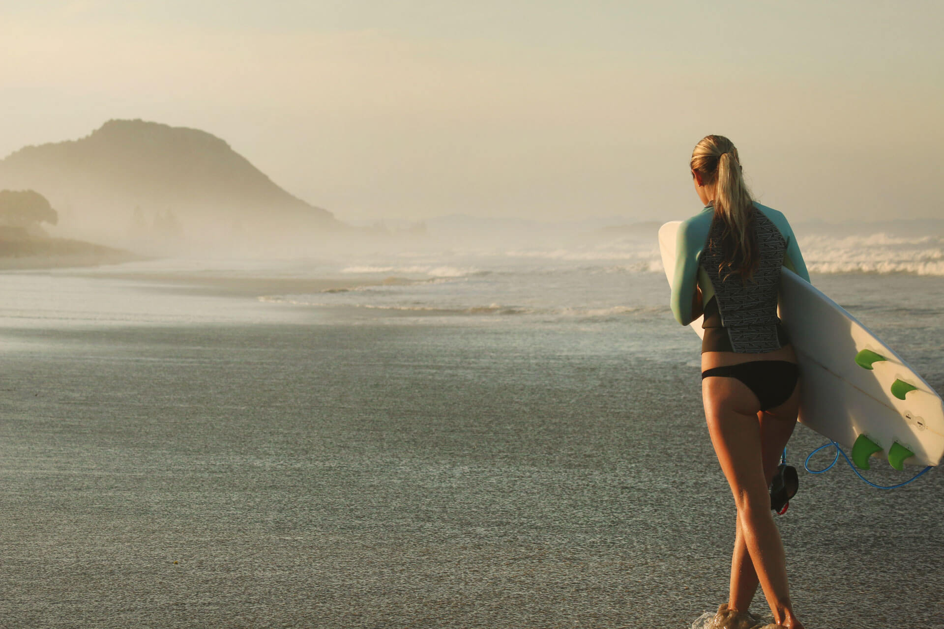 Sprachreisende mit Surfbrett am Strand von Mount Maunganui in Neuseeland