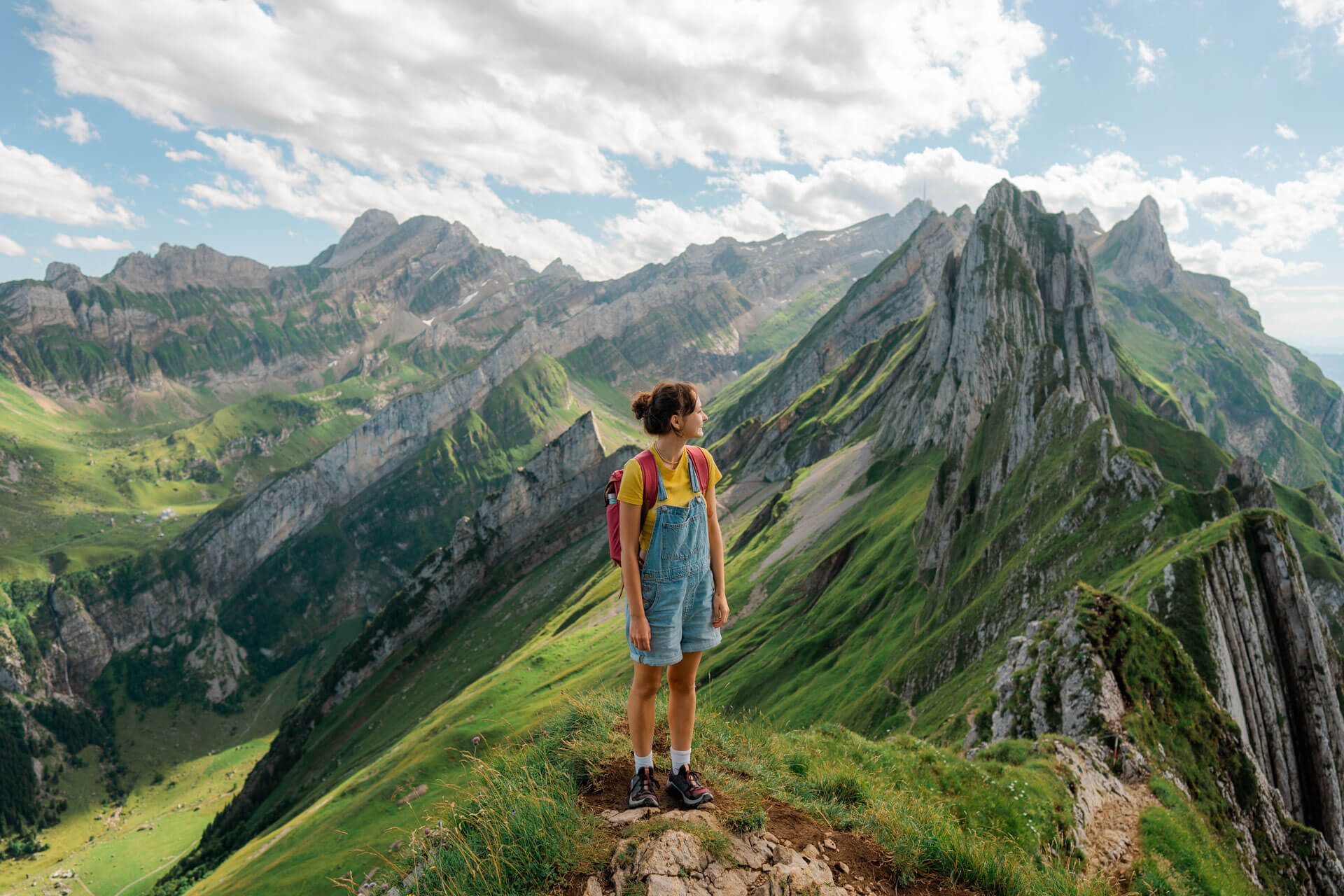 Person steht auf einem Bergpfad mit beeindruckendem Blick auf die grünen Alpen und felsigen Gipfel der Schweiz