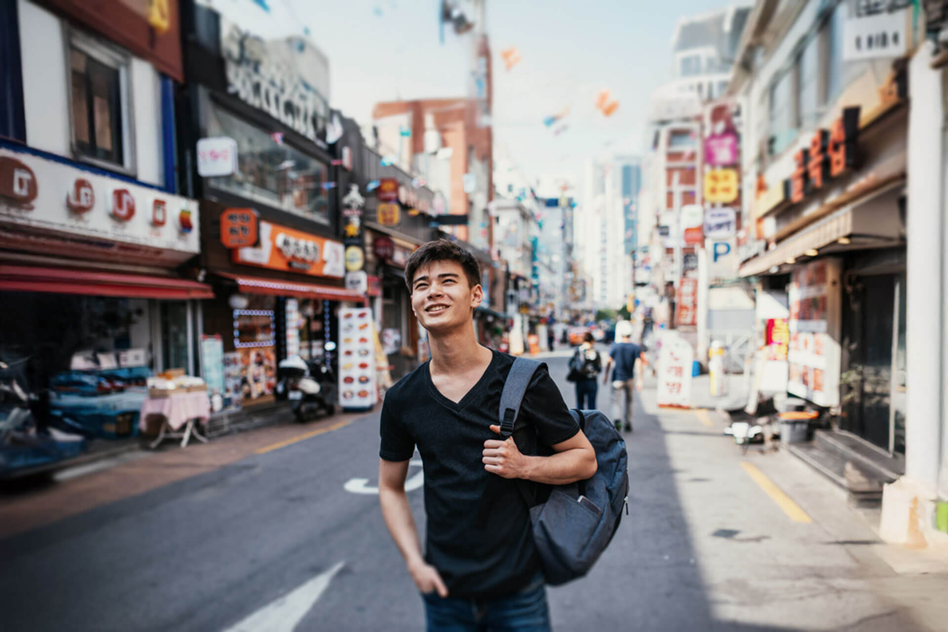 Person mit Rucksack schlendert durch eine belebte Einkaufsstraße in Seoul mit bunten Schildern und Geschäften