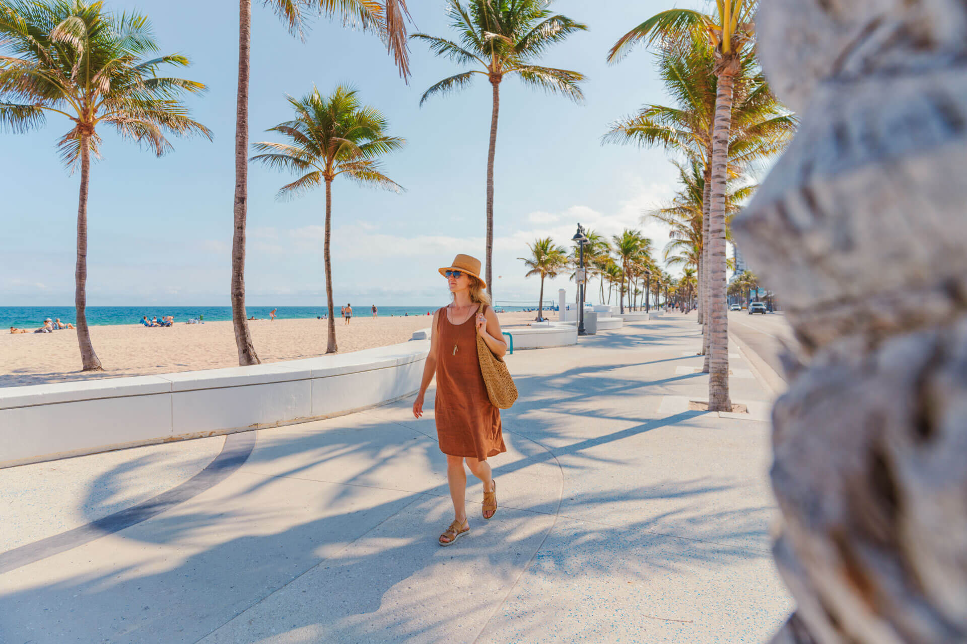 Spaziergängerin an der sonnigen Strandpromenade von Fort Lauderdale mit Palmen und Sandstrand