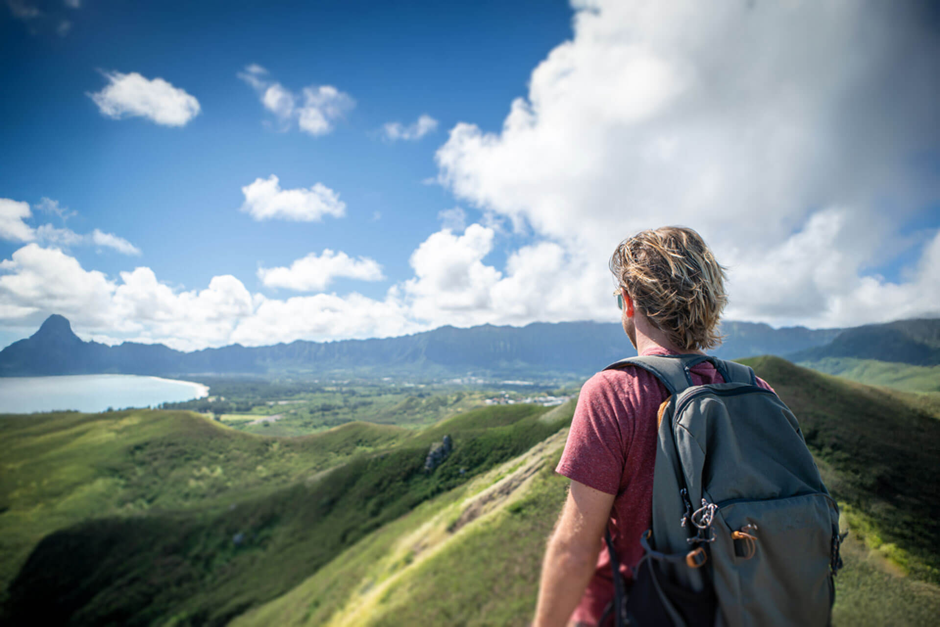 Sprachreisender mit Rucksack blickt über die grüne Küstenlandschaft von Oahu auf Hawaii