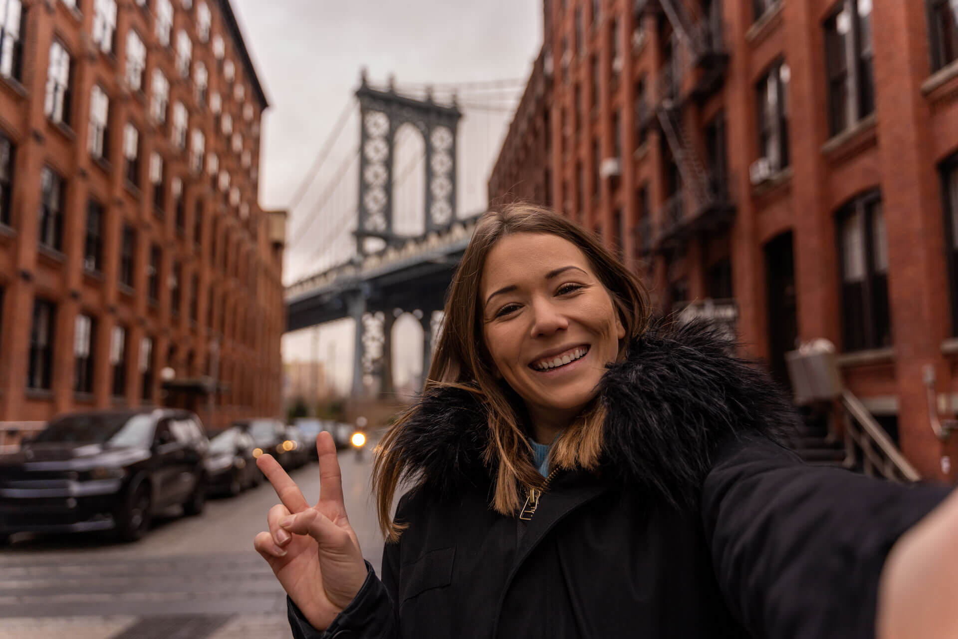 Junge Frau macht ein Selfie in Brooklyn mit Blick auf die Manhattan Bridge in New York