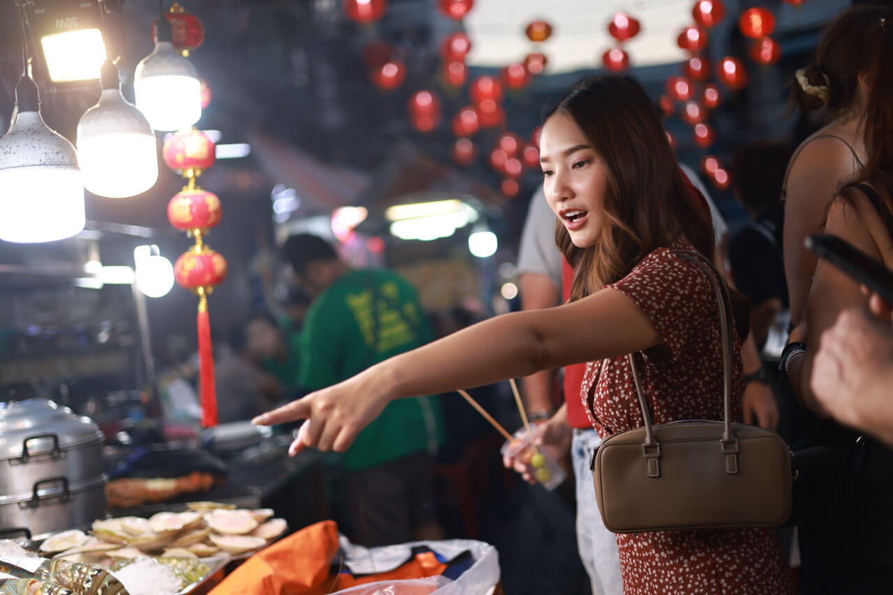 Reisende wählt Streetfood auf einem Nachtmarkt in Peking mit roten Laternen