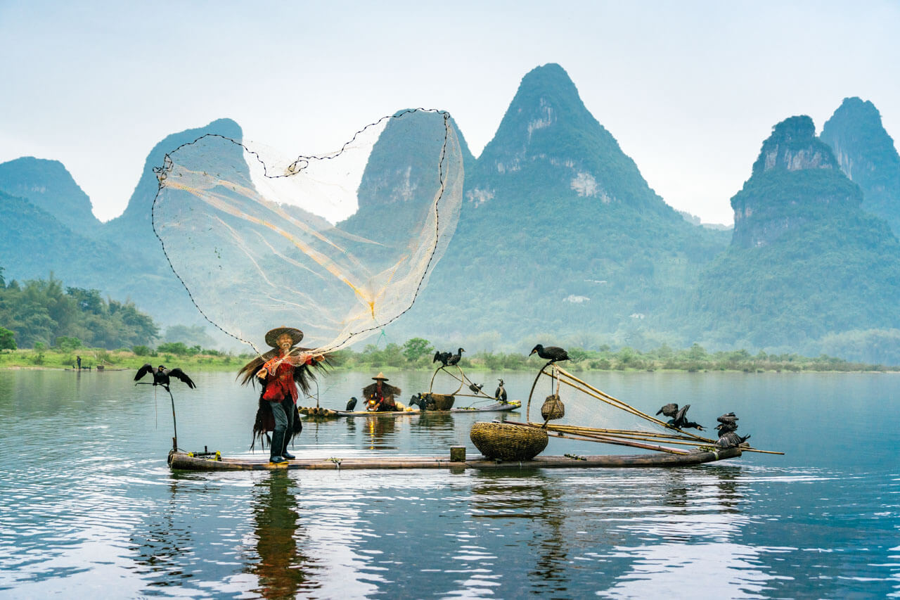 Traditioneller Fischer wirft Netz auf Fluss vor Karstbergen typisch für Kultur und Alltag in China