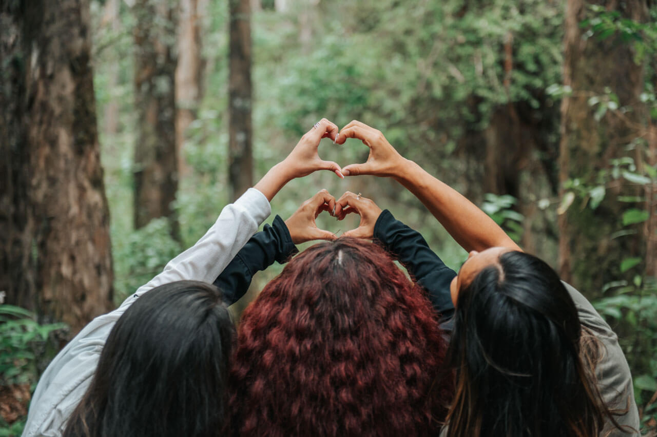 Drei Freundinnen im Regenwald von Costa Rica formen mit den Händen Herzen als Symbol für Freundschaft.