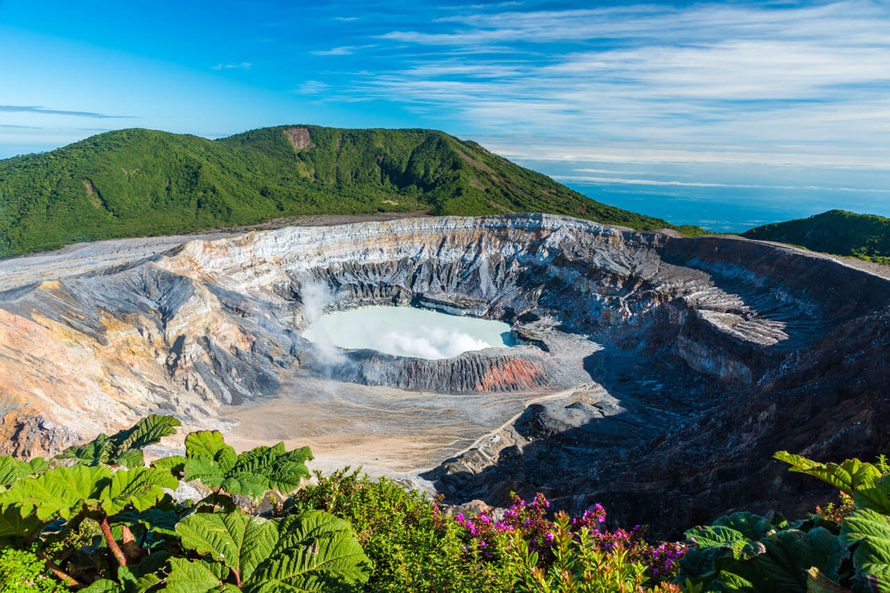 Krater des aktiven Vulkans Poás in Costa Rica mit dampfendem Kratersee, umgeben von grüner Landschaft.