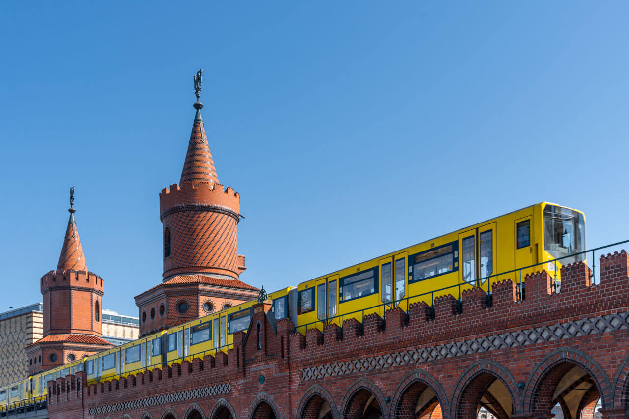 Gelbe U-Bahn fährt über die Oberbaumbrücke mit roten Backsteintürmen vor klarem Himmel.