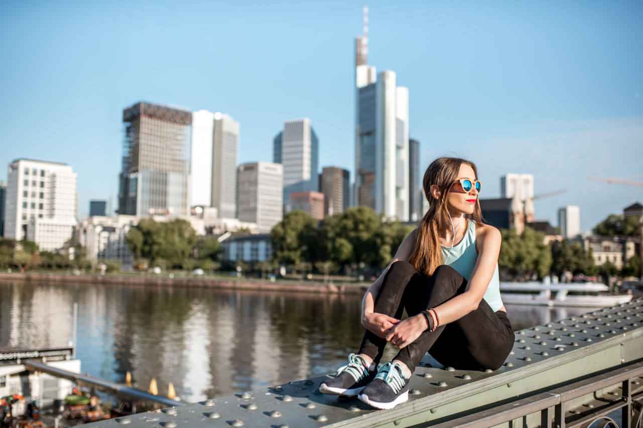 Junge Frau sitzt auf dem Eisernen Steg am Main und blickt zur Skyline, entspannte Sommerstimmung.