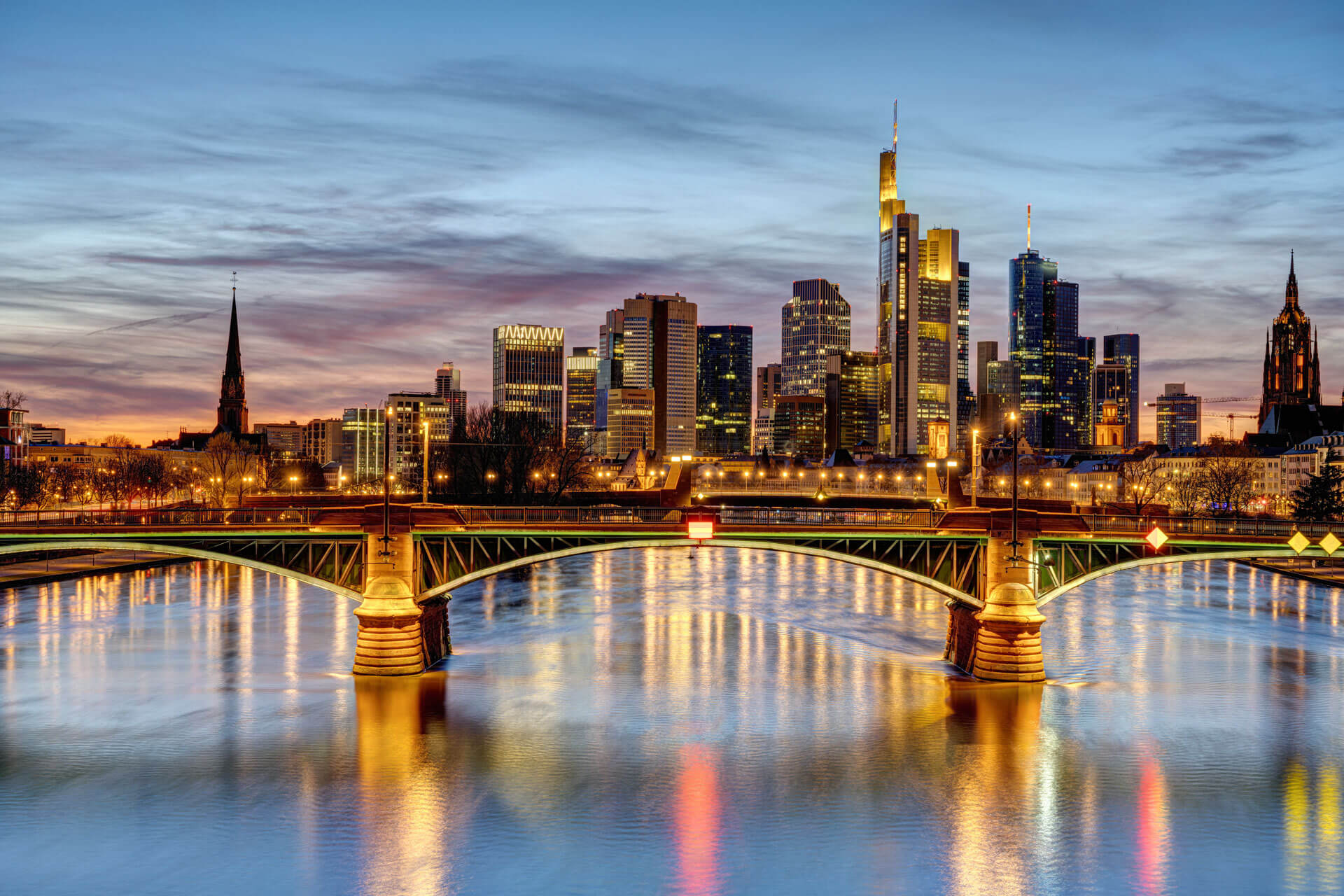 Abendstimmung an der Frankfurter Skyline mit beleuchteter Brücke über den Main.