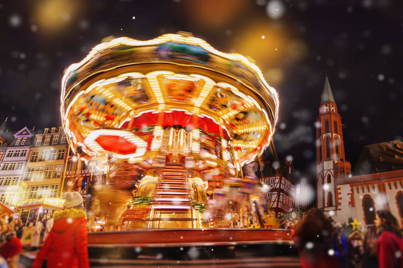 Leuchtendes Karussell auf dem Weihnachtsmarkt am Römerberg, Fachwerk und Kirche im Hintergrund.