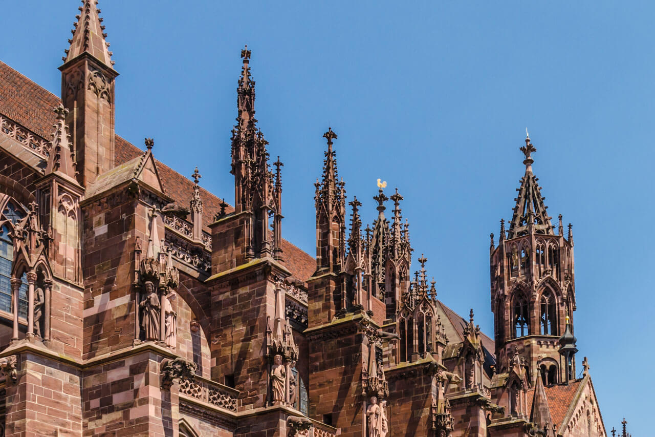 Gotische Details und Türme des Freiburger Münsters vor blauem Himmel.