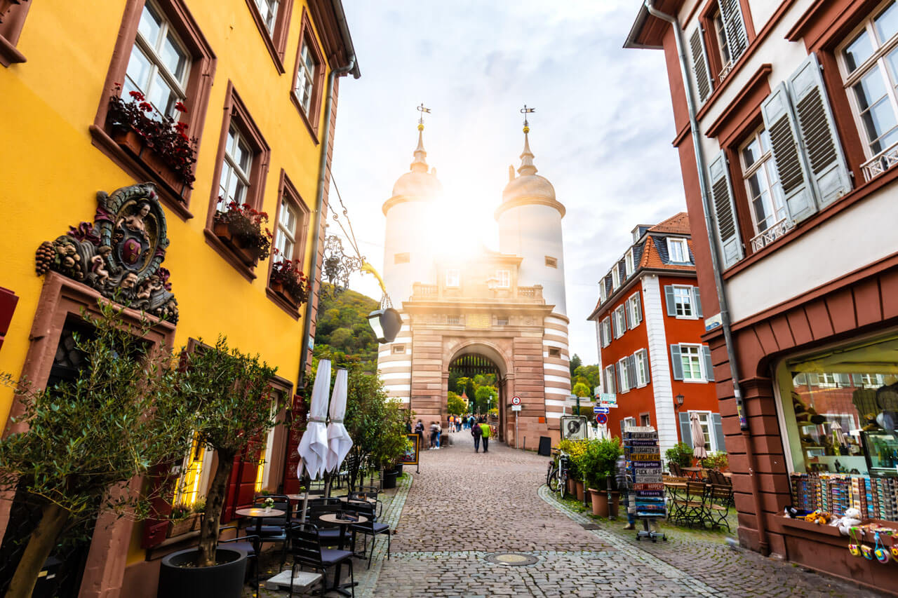 Historisches Stadttor zwischen bunten Häusern, Kopfsteinpflastergasse mit Cafés und Sonnenlicht