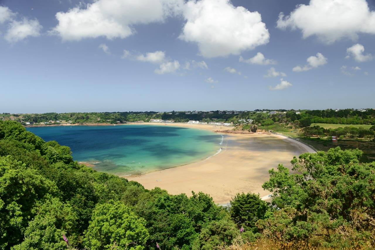 Saint Brelade’s Bay auf Jersey mit türkisblauer Bucht und Sandstrand umgeben von Grün. Ort für Gespräche mit Locals und lockeren Sprachkurs am Strand.