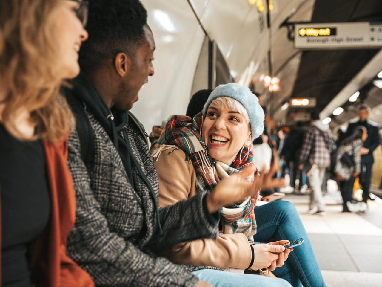 Freunde unterhalten sich lachend auf dem Bahnsteig der London Underground Konversation und spontane Reaktionen im Alltagstraining verbessern