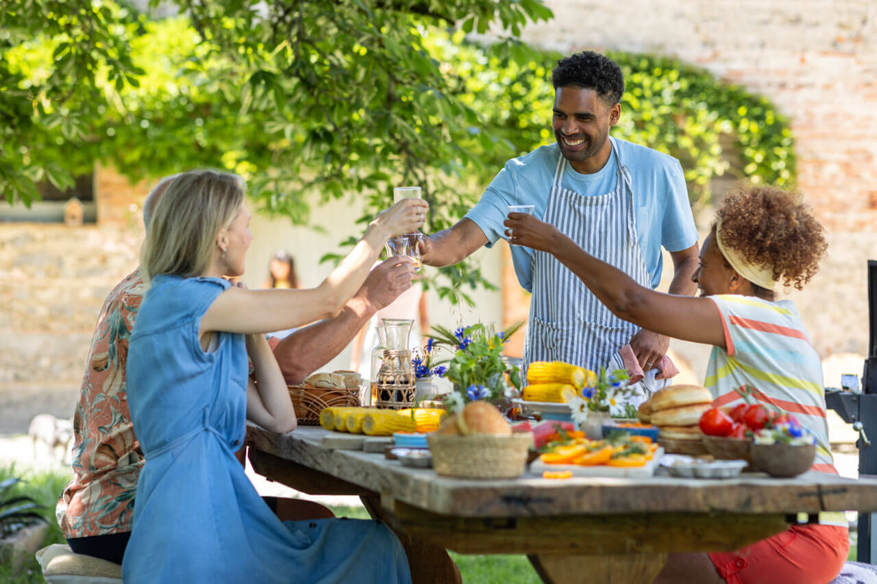 Menschen stoßen beim Sommeressen im Garten an Grammatik üben im Sprachkurs