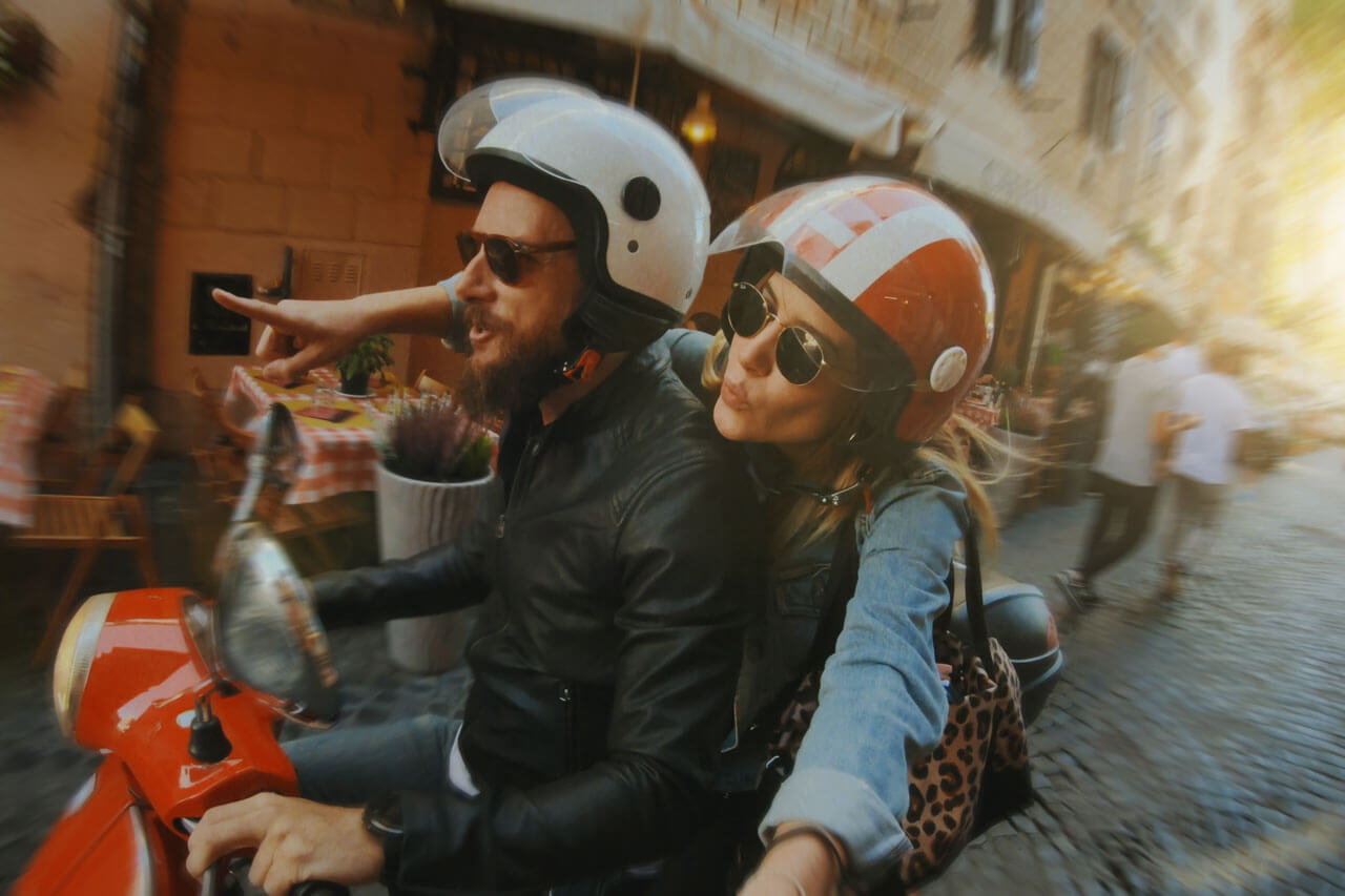 Paar auf einem Roller fährt durch die Straßen Mailands, typisch italienisches Flair für eine Sprachreise.