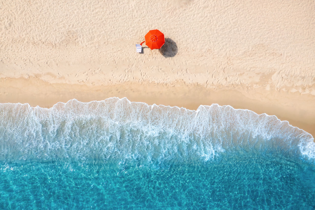 Roter Sonnenschirm am Sandstrand mit türkisblauem Meer Hörverstehen trainieren im Sprachkurs
