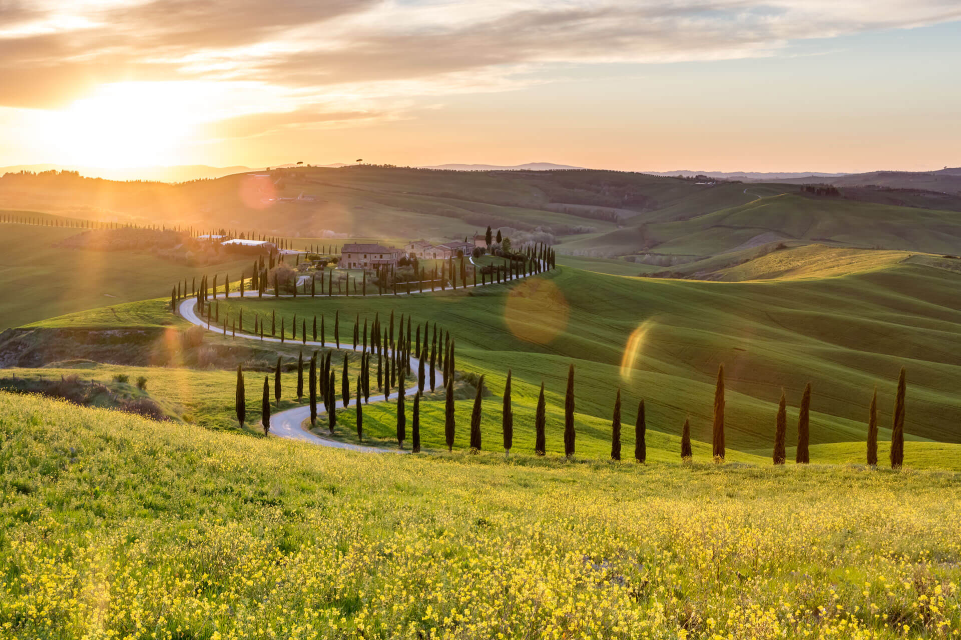 Sonnenuntergang über den sanften Hügeln der Toskana mit gewundener Zypressenallee.