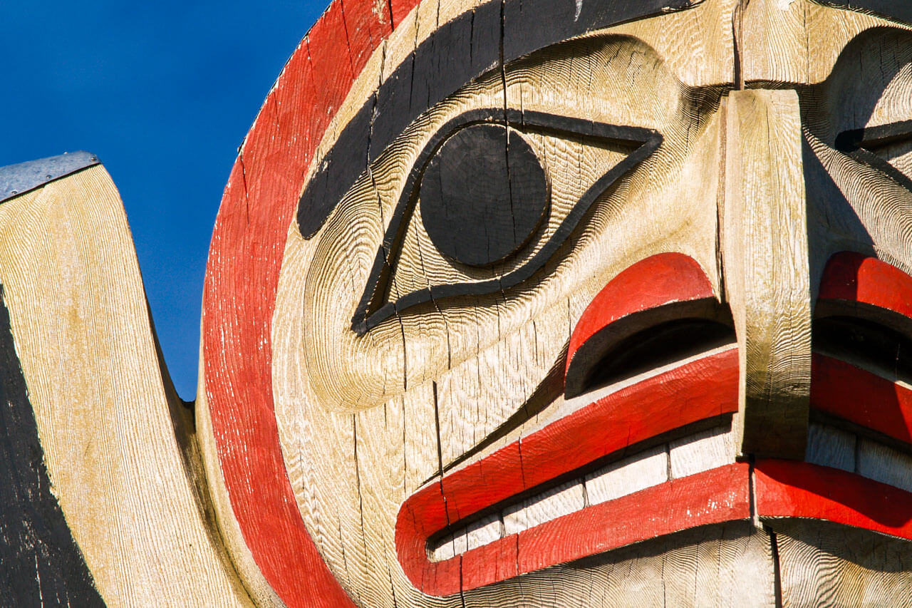 Detail eines geschnitzten Totempfahls vor blauem Himmel, auf Sprachkurs in Kanada.