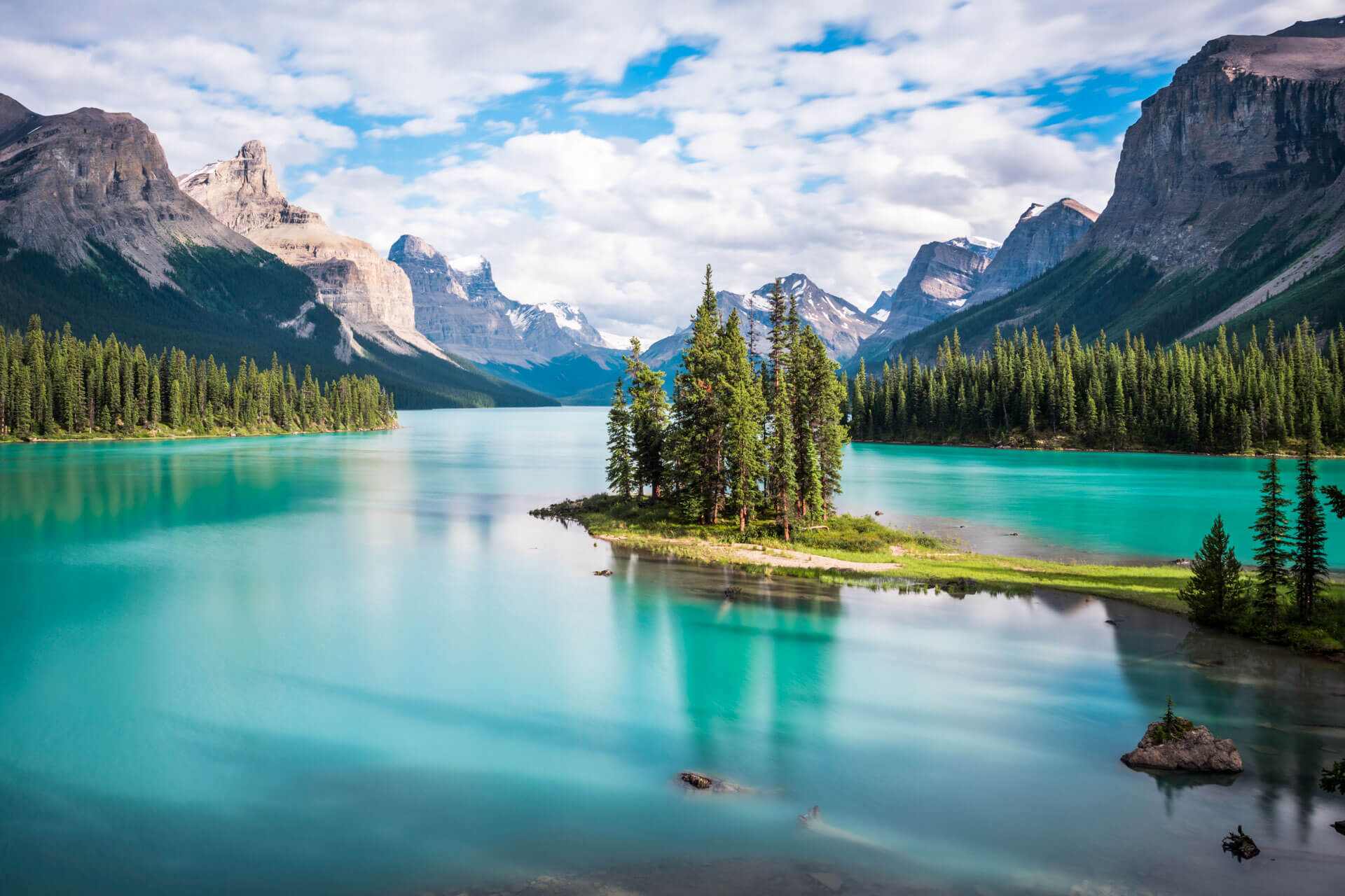 Blick auf den türkisblauen See im Jasper Nationalpark mit bewaldeter Insel und Bergpanorama.
