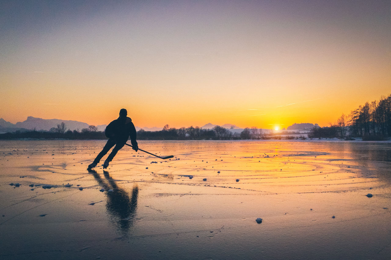 Eishockeyspieler auf zugefrorenem See bei Sonnenuntergang, Konversation üben in der Freizeit.