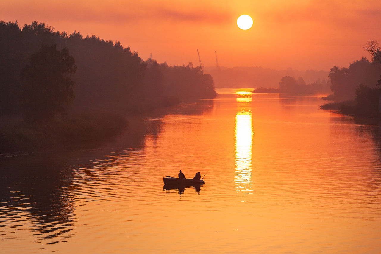 Silhouetten zweier Menschen im Ruderboot angeln auf einem Fluss bei intensivem Sonnenuntergang