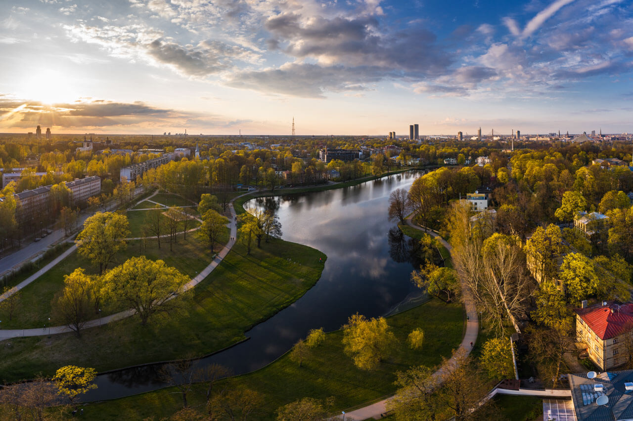 Luftaufnahme eines geschwungenen Stadtparks mit See und Wegen in Riga Abendsonne und weite Aussicht