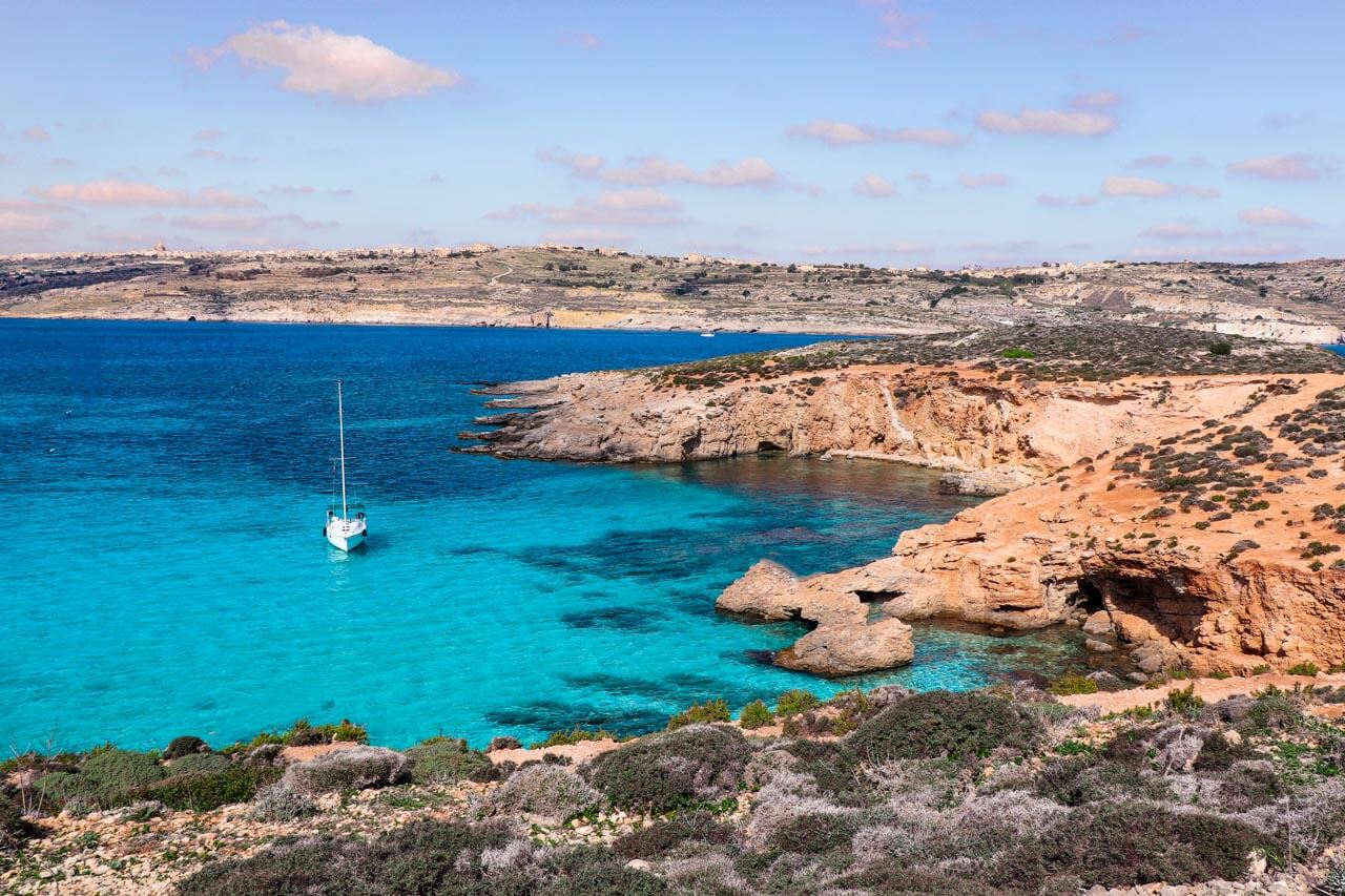 Türkisblaue Bucht mit Segelboot und Felsküste, Exkursion nach dem Unterricht. Vokabeln im Alltag anwenden.