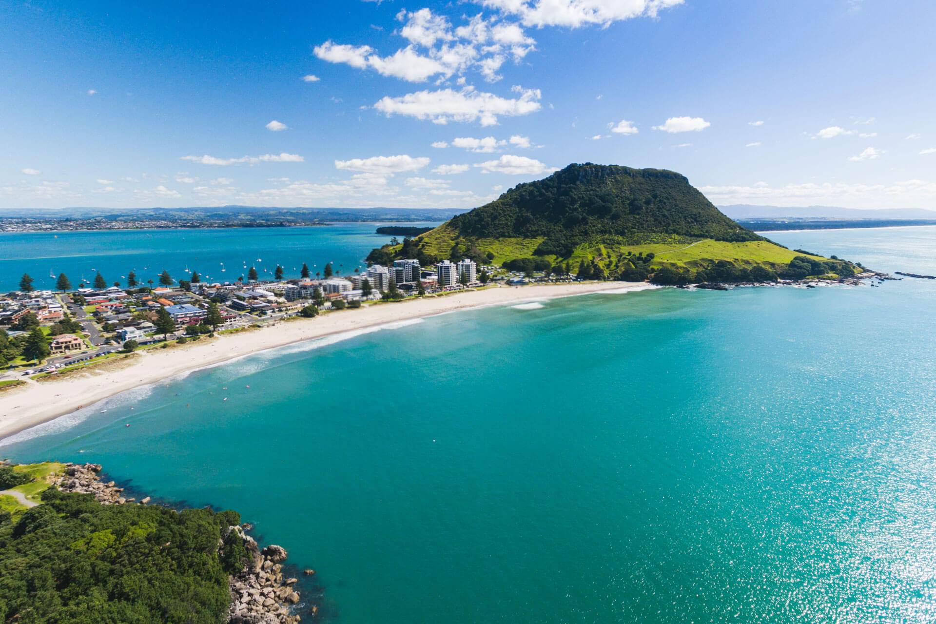 Breiter Strand mit türkisfarbenem Wasser und grünem Berg, Sprachreise am Pazifik in Mount Maunganui.