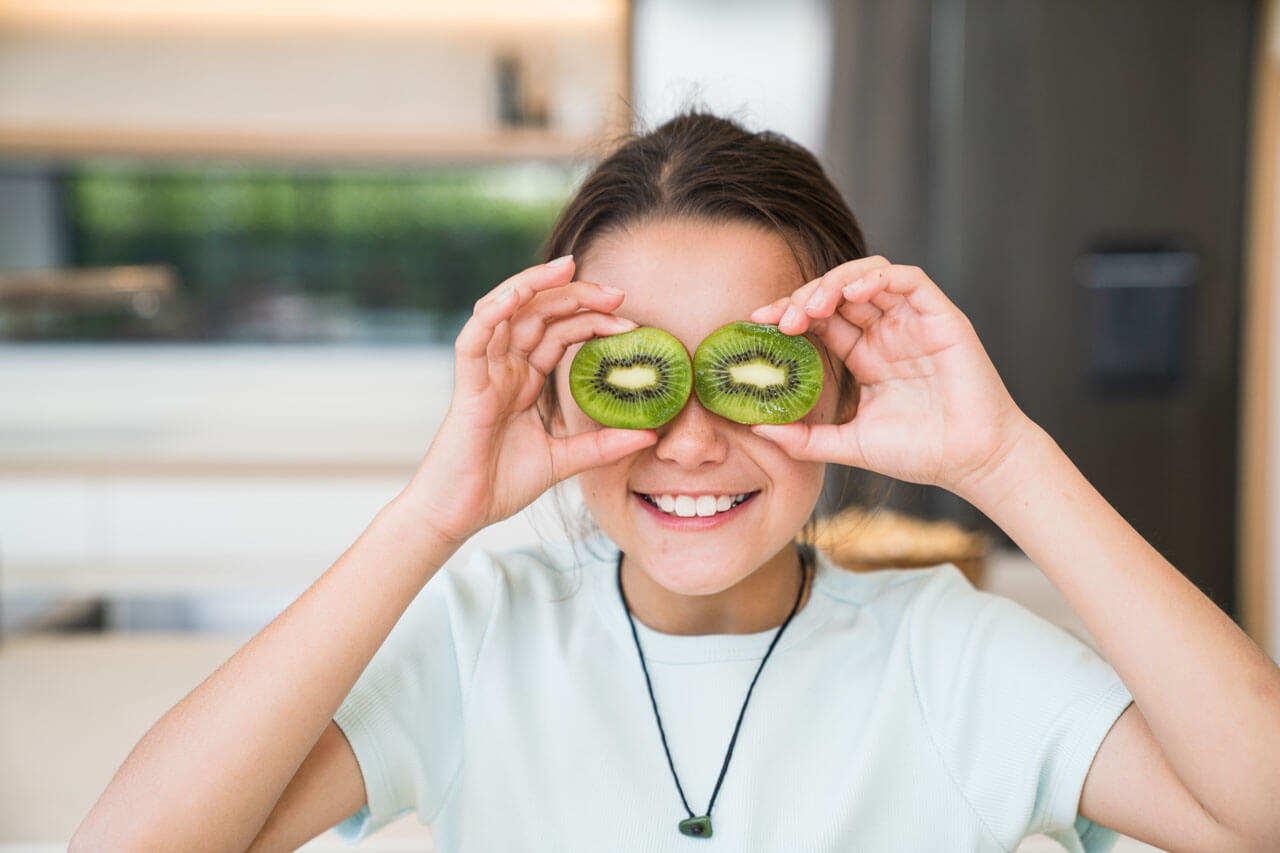 Person hält Kiwischeiben vor die Augen und lacht, Vokabeln üben im Alltag.