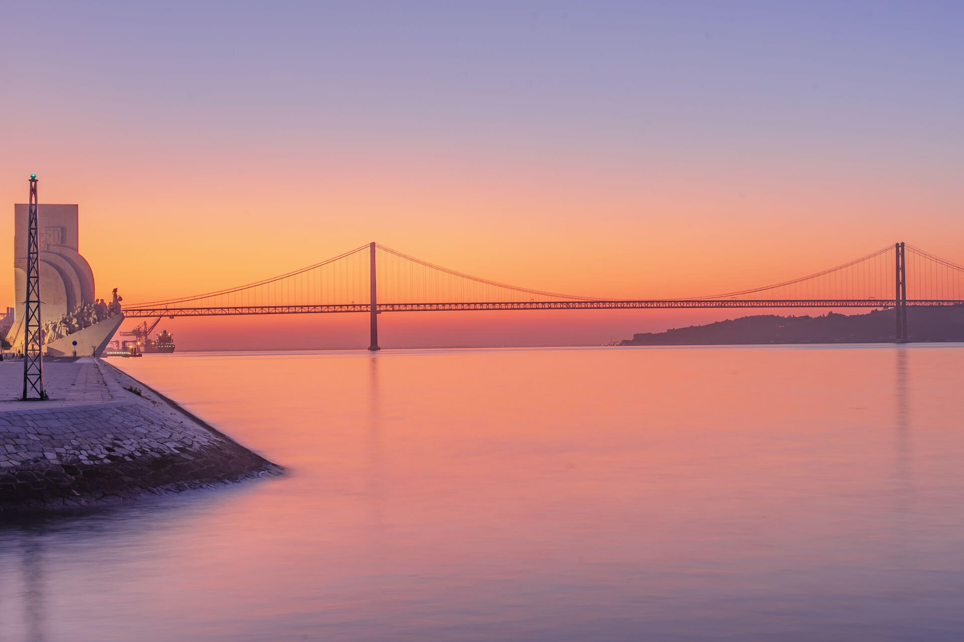 Sonnenaufgang über der Brücke des 25. April in Lissabon mit Blick auf das Entdeckerdenkmal – Sprachreise Portugal