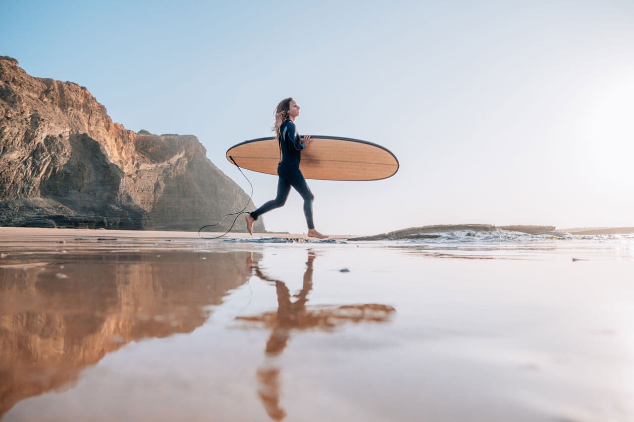 Surferin läuft mit Surfbrett am Strand Portugal Sprachreise Konversation üben