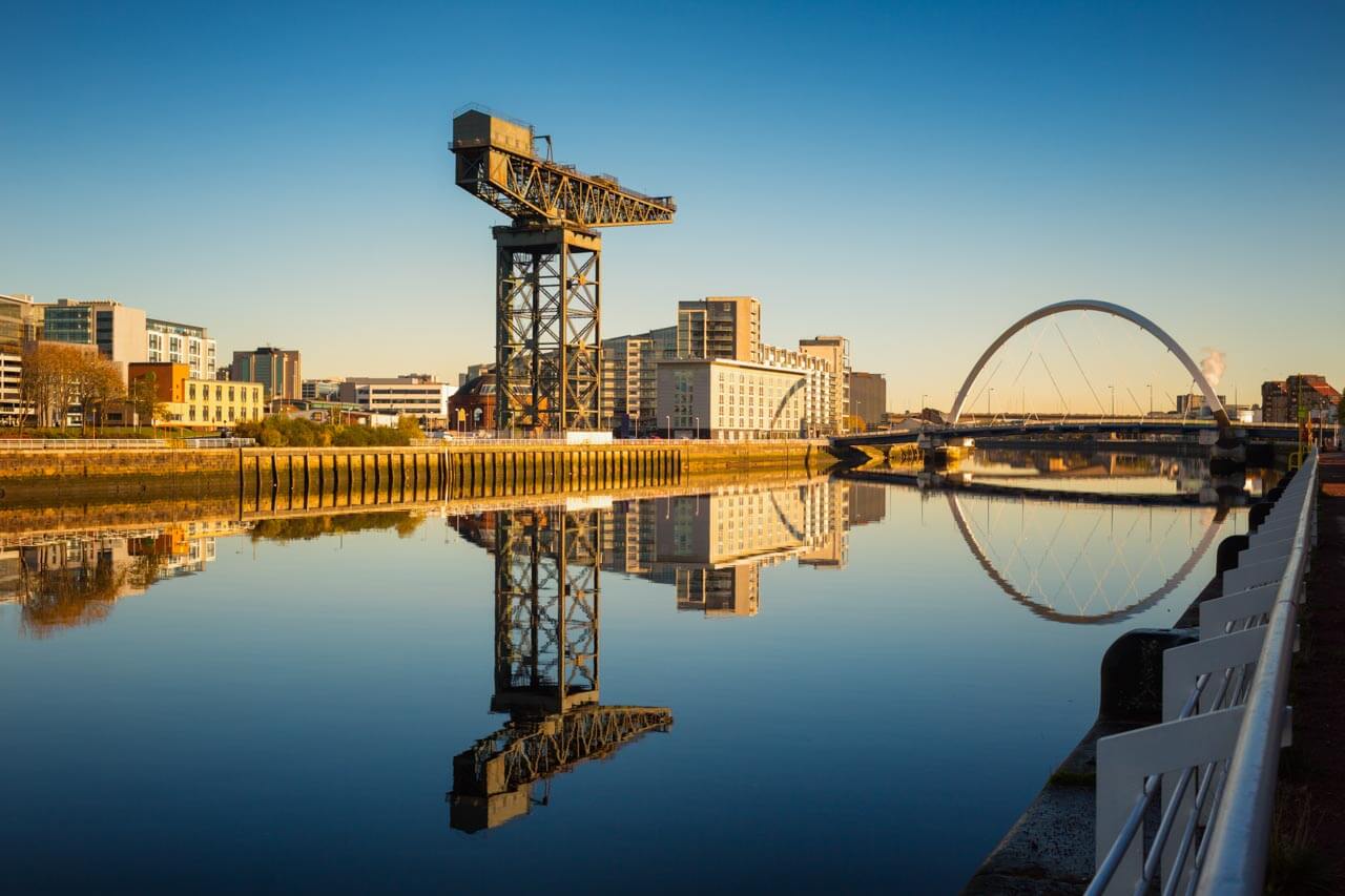 Industriekran und Brücke spiegeln sich im ruhigen Fluss bei Sonnenaufgang. Sprachkurs in Glasgow.